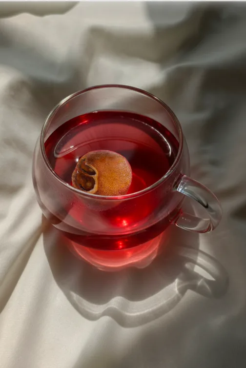 Glass cup of red hibiscus tea on light fabric